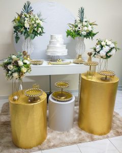 Decoração decasamento branco e dourado, com arranjos florais grandes cor champanhe, bandejas douradas com pedrarias, mesa branca de madeira grande e cilindros metalizados na cor dourada.